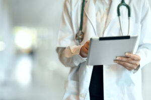 a medical professional holds a tablet while reviewing their work on electronic medical record software