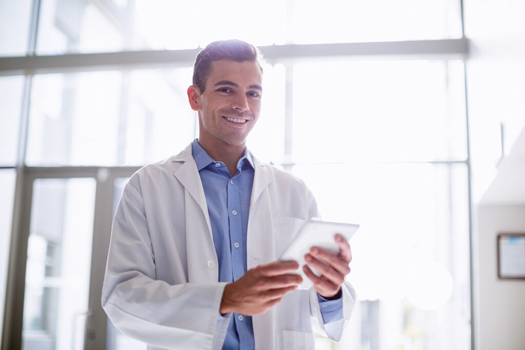 medical professional smiles while holding and typing on a tablet