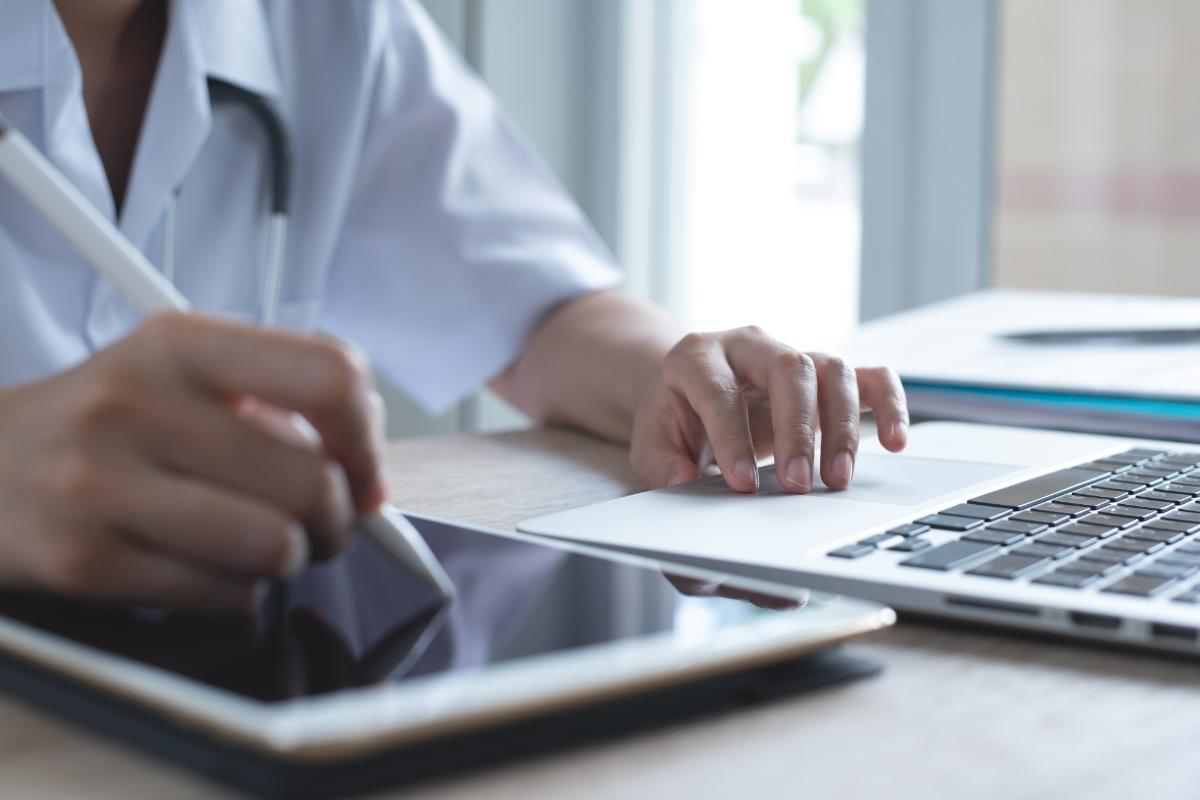 medical professional typing on laptop while making notes on tablet and demonstrating how EMR improves patient safety and reduces medical errors