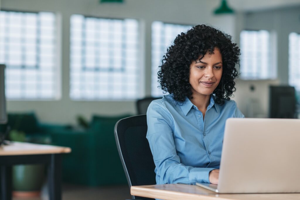 Professional woman sitting at a desk in a modern office, focused on working on her laptop